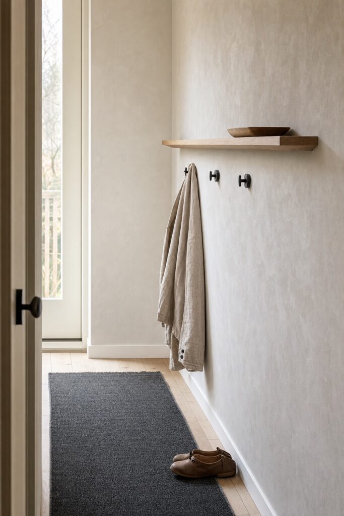 Small Japandi entryway with pale plaster walls, an oak ledge and a dark runner on the floor