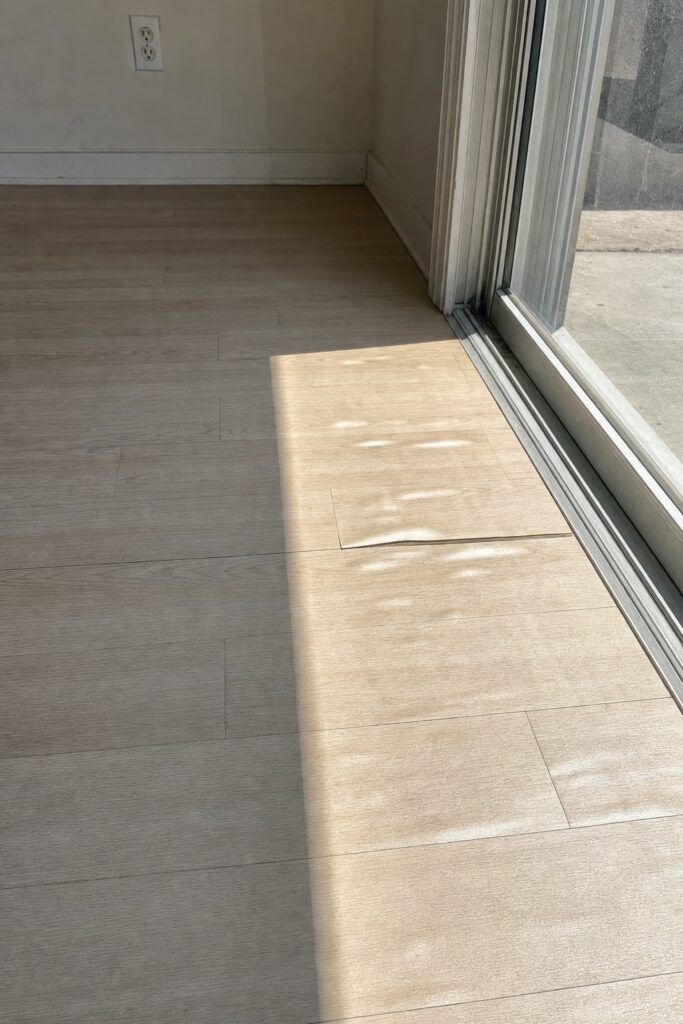 Peel and stick floor tiles bubbled and shifted in a bright stripe of sunlight near a patio door