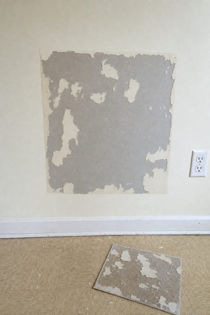 Wall area where a peel and stick tile has been removed taking patches of paint off with it
