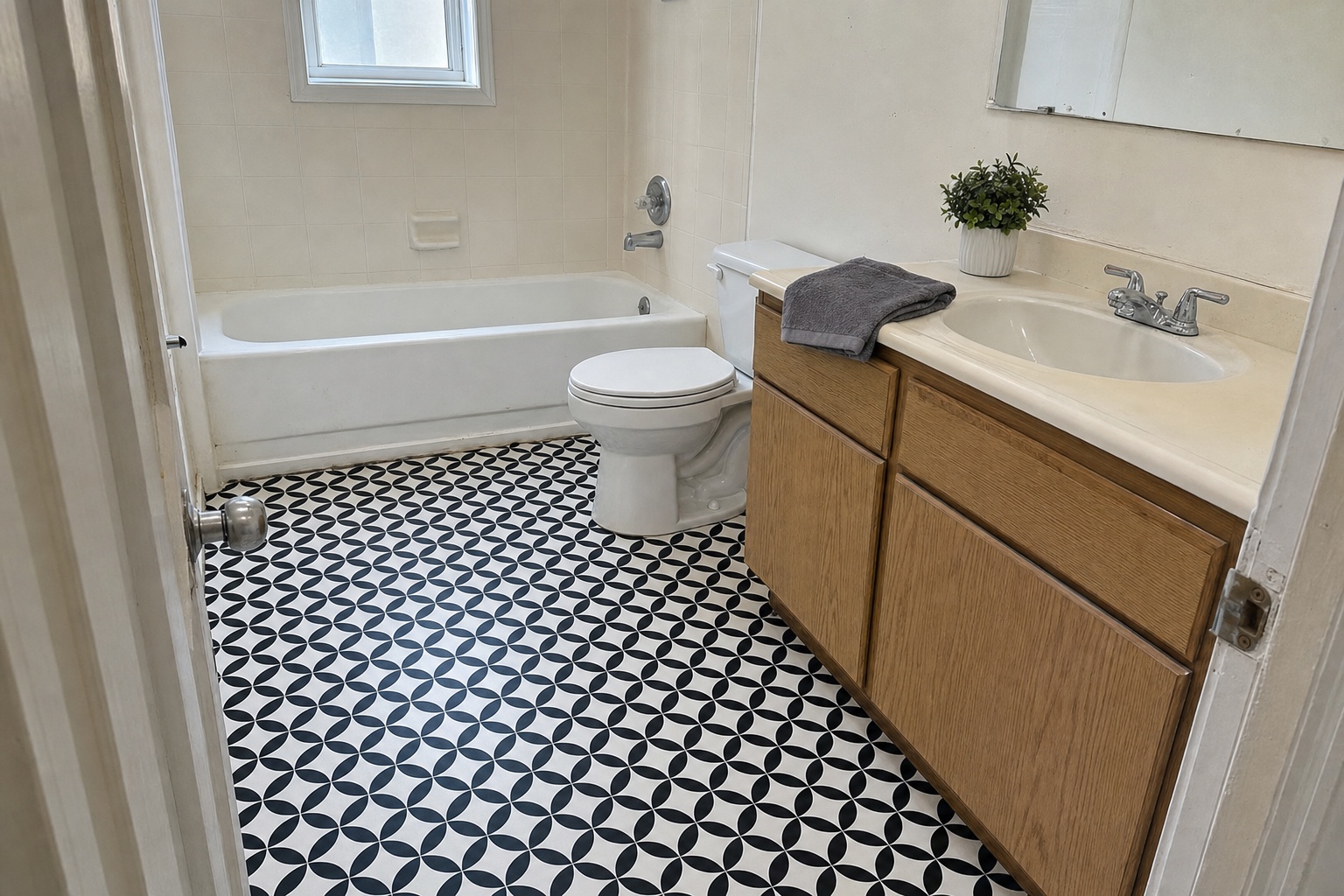 Small apartment bathroom floor covered in neatly laid black and white peel and stick tile with the original fixtures around it