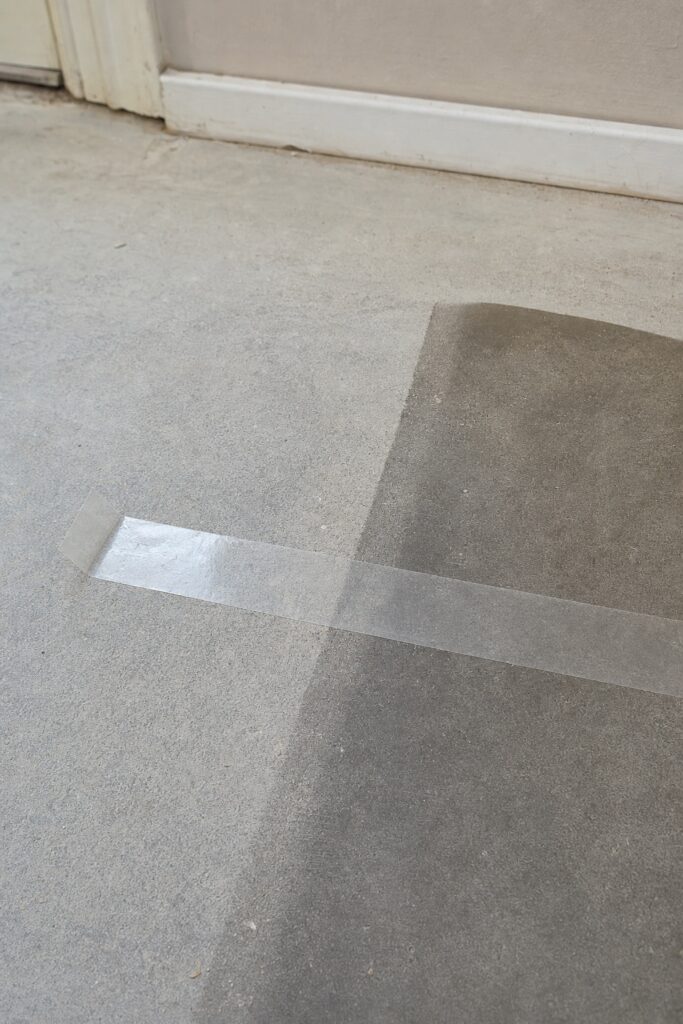 Strip of clear packing tape pressed onto a bare floor as an adhesion test with the surface clearly visible