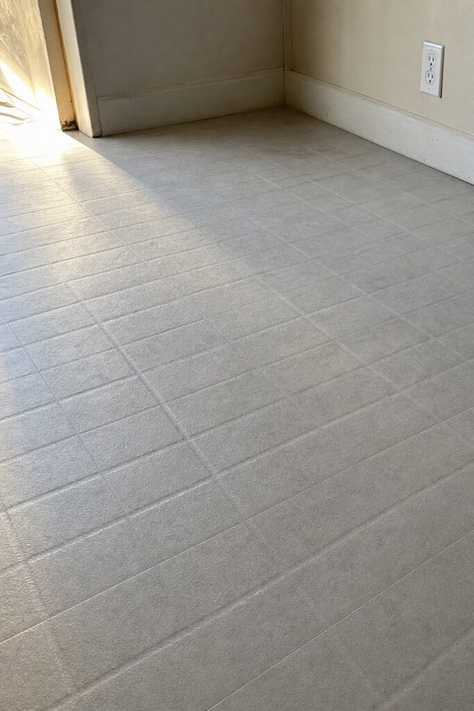 Peel and stick vinyl floor showing the grid of old grout lines pressing through its surface