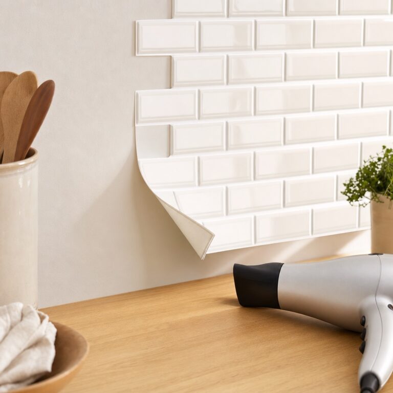 A white peel-and-stick tile sheet lifting from a wall corner with a hairdryer resting on the counter