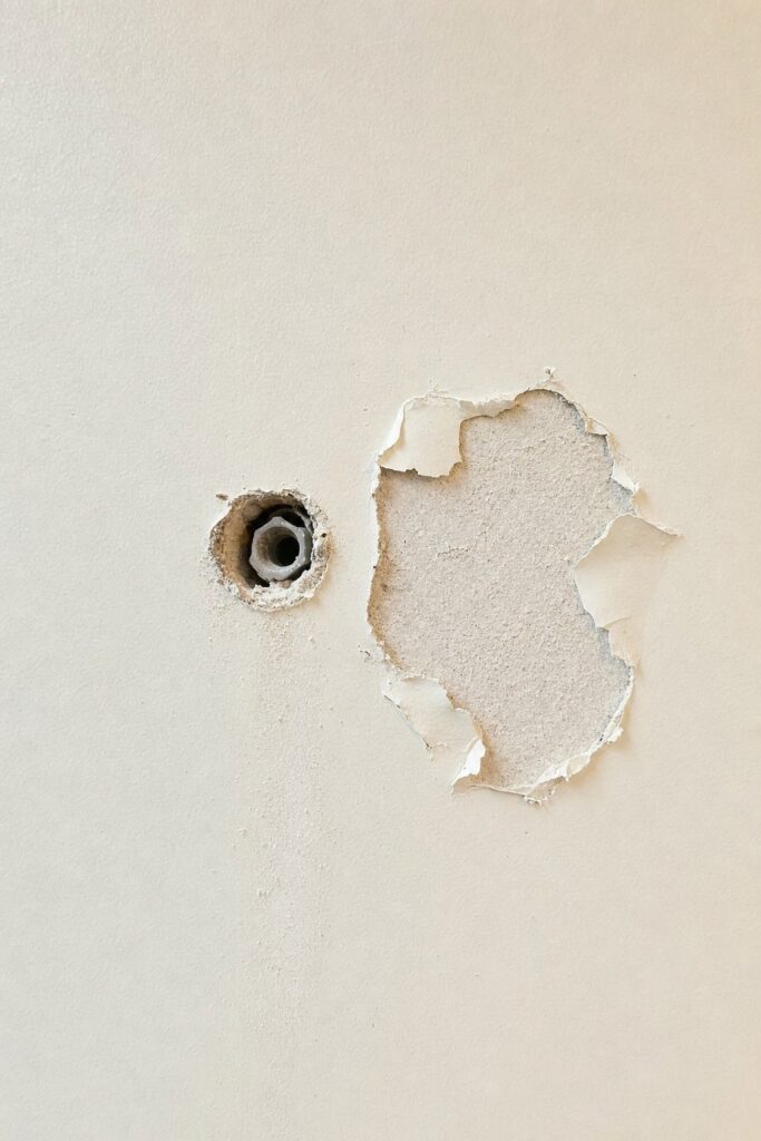 Rental wall left with an open drywall anchor hole and a patch of torn paper facing after a fixing was removed