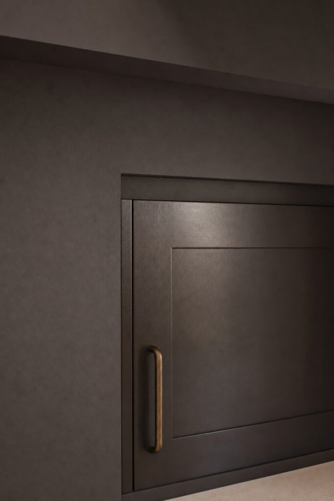 Close view of a dark satin cabinet door catching a soft highlight beside the matte painted wall above it