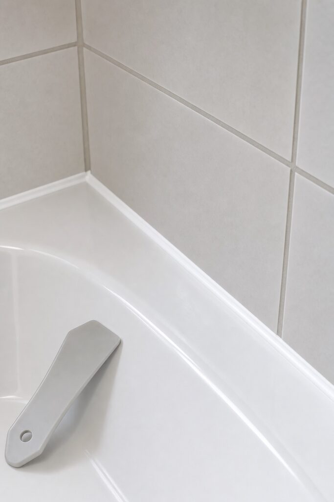 Close view of a clean new white caulk bead where a bathtub meets tiled wall with freshly whitened grout