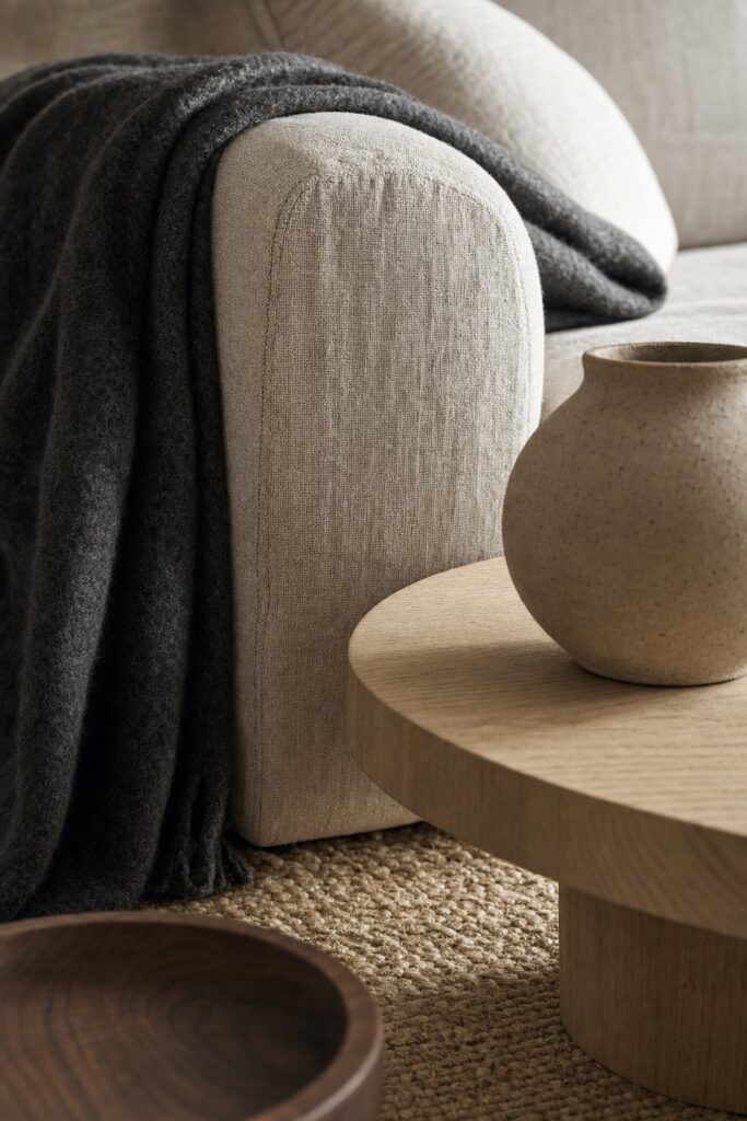 Close japandi texture stack of linen sofa fabric, wool throw, oak table edge, unglazed ceramic and jute rug in warm neutrals