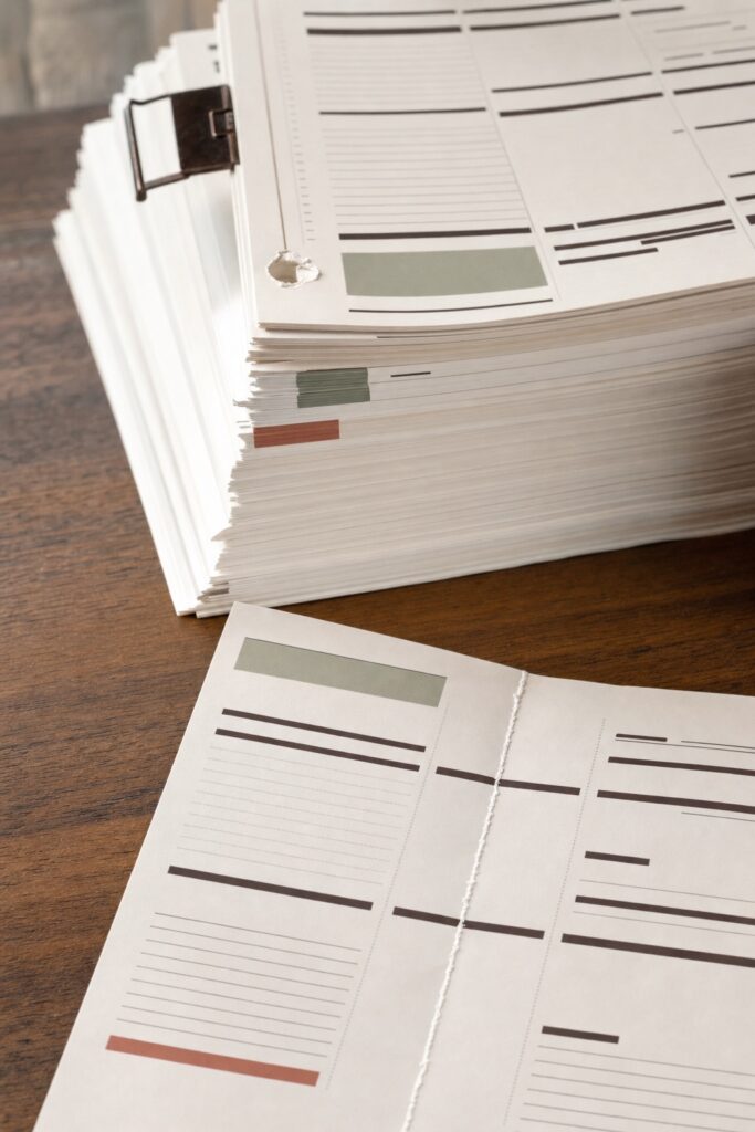 Thick stack of unused printed planner pages beside a folded page showing a cracked white line along its spine