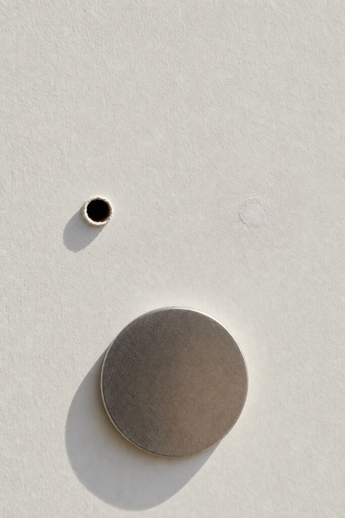 An open nail hole in a wall beside the same hole filled and sanded almost invisible, with a blank disc for scale