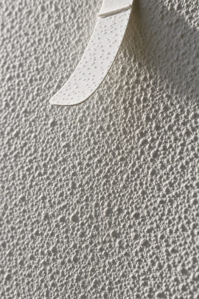 Raking light across an orange peel textured wall showing the bumps adhesive strips cannot grip