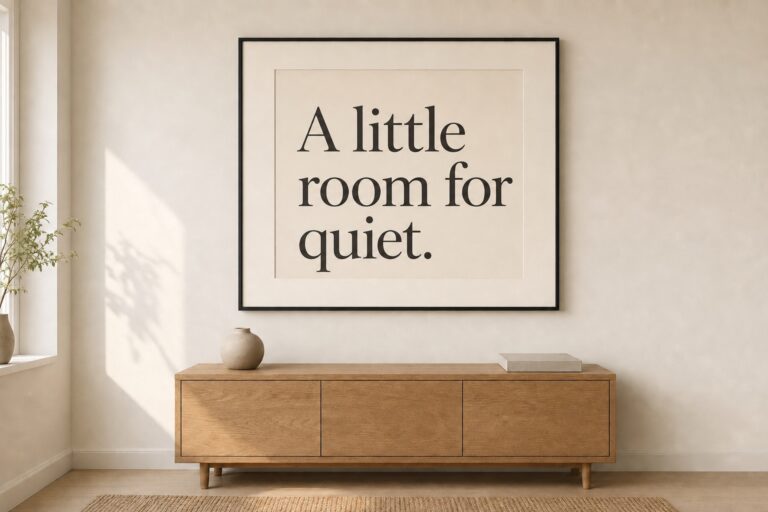 A black framed print reading “A little room for quiet.” above an oak sideboard in a softly lit room.